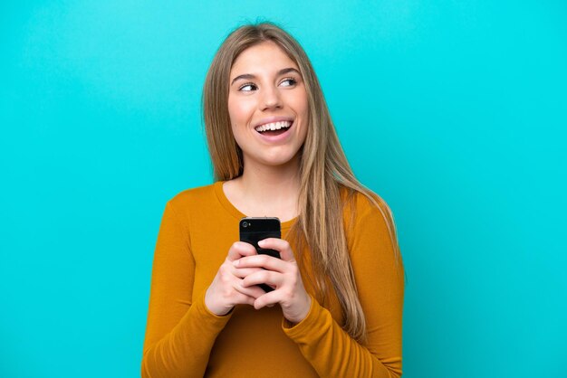 Jonge blanke vrouw geïsoleerd op blauwe achtergrond met behulp van mobiele telefoon en opzoeken