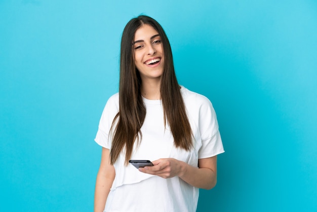 Jonge blanke vrouw geïsoleerd op blauwe achtergrond met behulp van mobiele telefoon