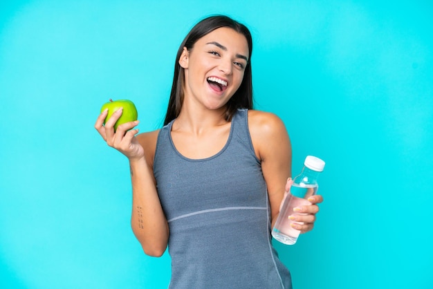 Jonge blanke vrouw geïsoleerd op blauwe achtergrond met een appel en met een fles water