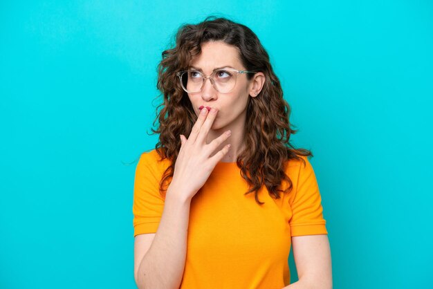Jonge blanke vrouw geïsoleerd op blauwe achtergrond Met een bril en twijfels