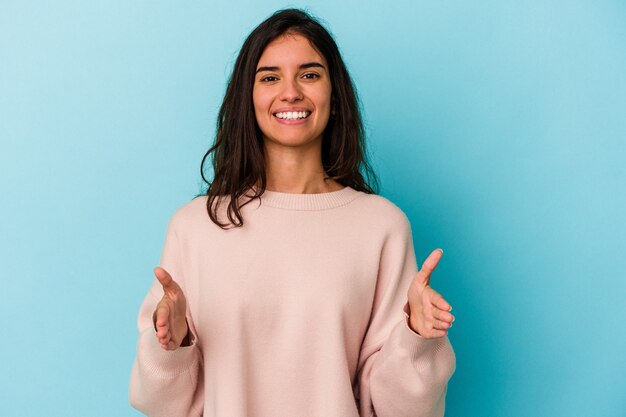 Jonge blanke vrouw geïsoleerd op blauwe achtergrond met iets met beide handen, productpresentatie.