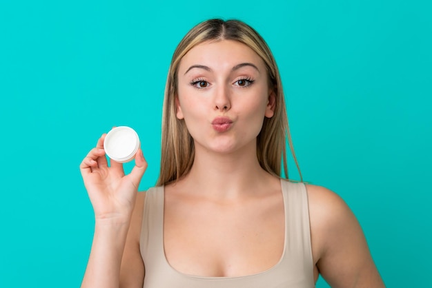 Jonge blanke vrouw geïsoleerd op blauwe achtergrond met moisturizer