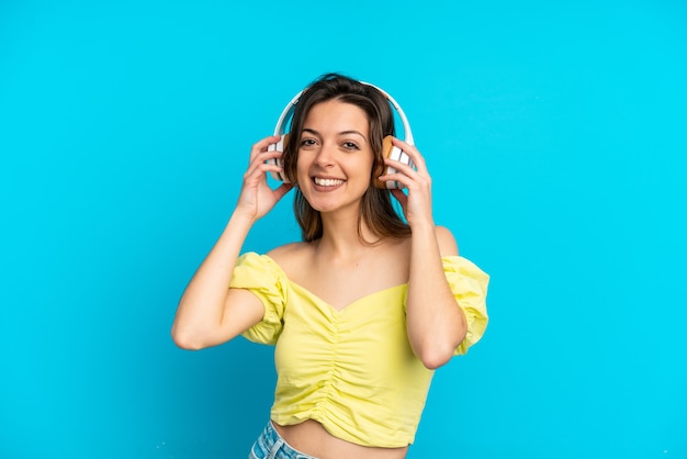 Jonge blanke vrouw geïsoleerd op blauwe achtergrond muziek luisteren
