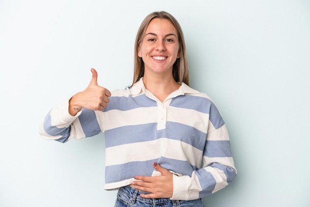 Jonge blanke vrouw geïsoleerd op blauwe achtergrond raakt buik aan, glimlacht zachtjes, eet- en tevredenheidsconcept.