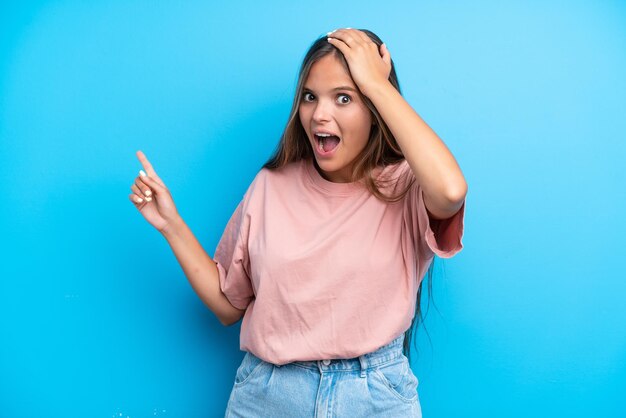 Jonge blanke vrouw geïsoleerd op blauwe achtergrond verrast en wijzende vinger naar de zijkant