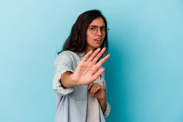 Jonge blanke vrouw geïsoleerd op blauwe achtergrond wordt geschokt door een dreigend gevaar