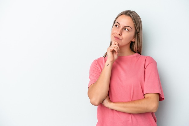 Jonge blanke vrouw geïsoleerd op blauwe achtergrond zijwaarts kijkend met twijfelachtige en sceptische uitdrukking.