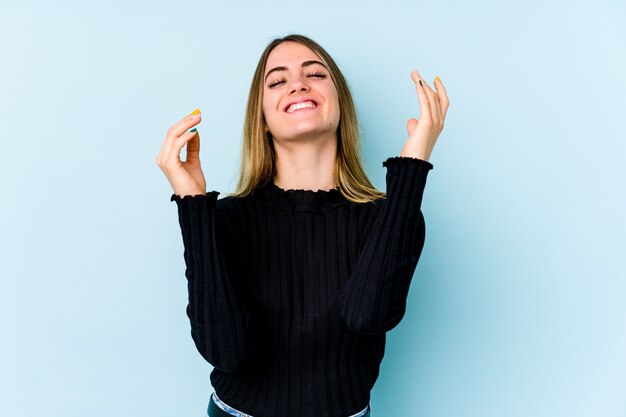 Jonge blanke vrouw geïsoleerd op blauwe muur blij lachen veel. Geluk concept.