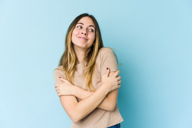 Jonge blanke vrouw geïsoleerd op blauwe muur knuffels, zorgeloos en gelukkig glimlachen.