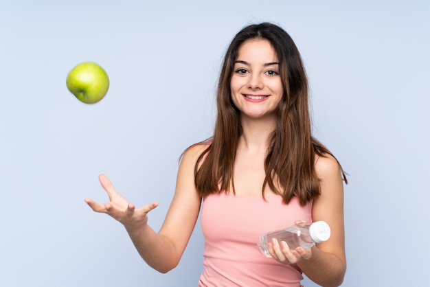 Jonge blanke vrouw geïsoleerd op blauwe muur met een appel en met een fles water