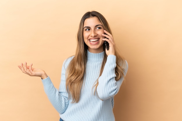 Jonge blanke vrouw geïsoleerd op een beige achtergrond die een gesprek voert met de mobiele telefoon met iemand