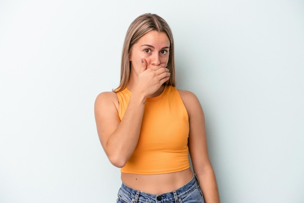 Jonge blanke vrouw geïsoleerd op een blauwe achtergrond die de mond bedekt met handen die bezorgd kijken.