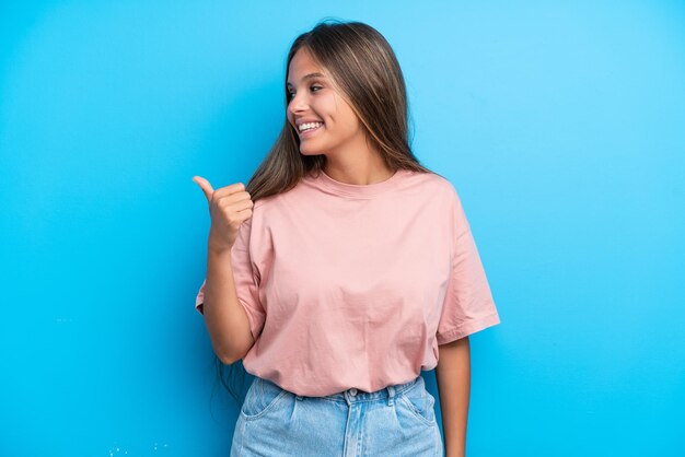 Jonge blanke vrouw geïsoleerd op een blauwe achtergrond die naar de zijkant wijst om een product te presenteren