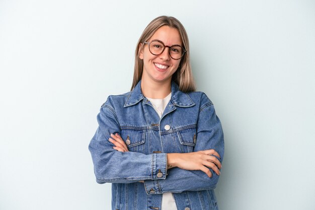 Jonge blanke vrouw geïsoleerd op een blauwe achtergrond die zich zelfverzekerd voelt en vastberaden de armen kruist.