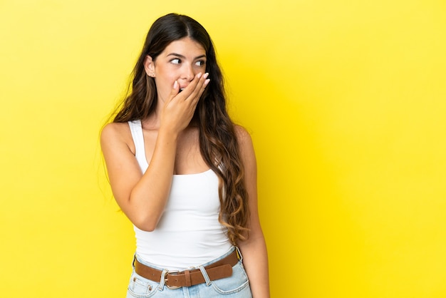 Jonge blanke vrouw geïsoleerd op een gele achtergrond die een verrassingsgebaar doet terwijl ze naar de zijkant kijkt