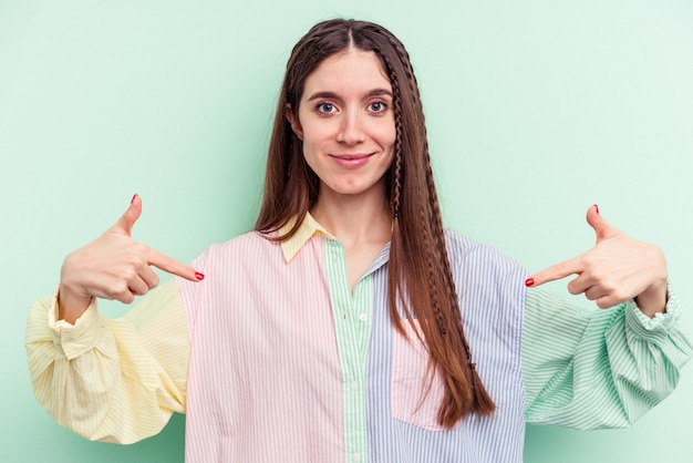 Jonge blanke vrouw geïsoleerd op een groene achtergrond persoon die met de hand wijst naar een ruimte voor een shirtkopie, trots en zelfverzekerd