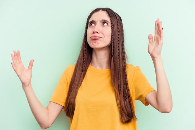 Jonge blanke vrouw geïsoleerd op een groene achtergrond schreeuwend naar de hemel en gefrustreerd omhoog kijkend