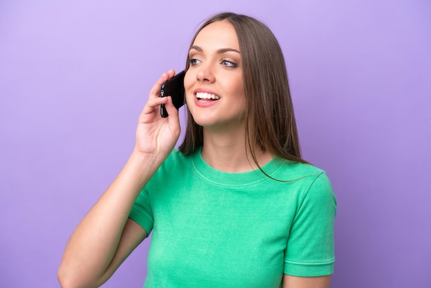 Jonge blanke vrouw geïsoleerd op een paarse achtergrond die een gesprek voert met de mobiele telefoon