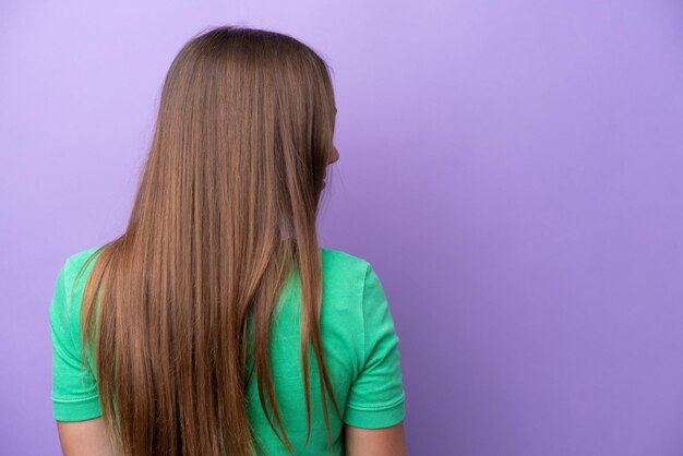 Jonge blanke vrouw geïsoleerd op een paarse achtergrond in de achterste positie en op zoek naar de zijkant