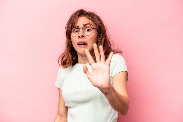 Jonge blanke vrouw geïsoleerd op een roze achtergrond wordt geschokt als gevolg van een dreigend gevaar