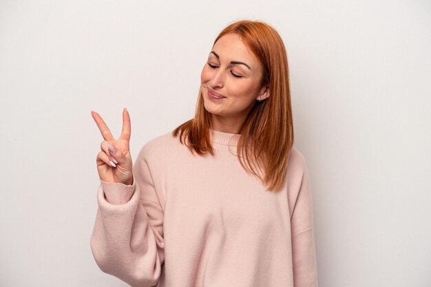 Jonge blanke vrouw geïsoleerd op een witte achtergrond blij en zorgeloos met een vredessymbool met vingers