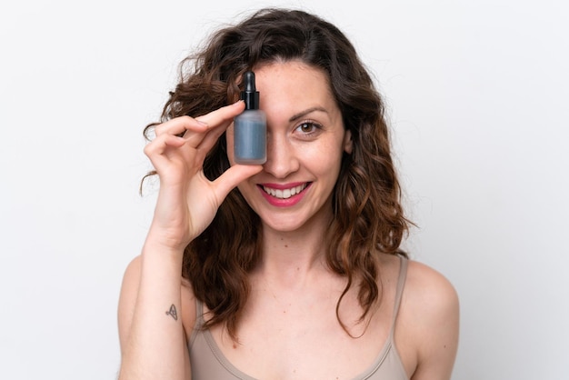 Jonge blanke vrouw geïsoleerd op een witte achtergrond die een serum vasthoudt terwijl ze lacht Close-up portret