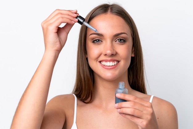 Jonge blanke vrouw geïsoleerd op een witte achtergrond die een serum vasthoudt terwijl ze lacht close-up portret