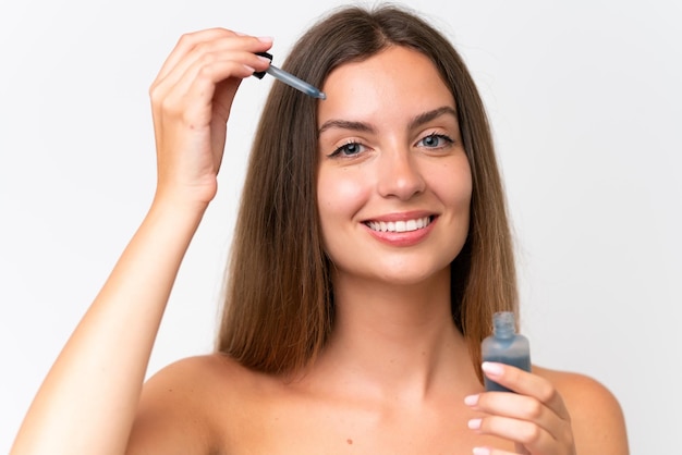 Jonge blanke vrouw geïsoleerd op een witte achtergrond die een serum vasthoudt terwijl ze lacht Close-up portret