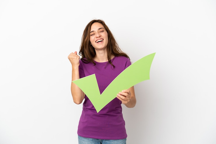 Foto jonge blanke vrouw geïsoleerd op een witte achtergrond die een vinkje houdt en een overwinning viert