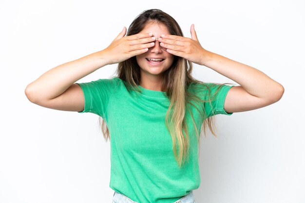 Jonge blanke vrouw geïsoleerd op een witte achtergrond die haar ogen met haar handen bedekt en glimlacht