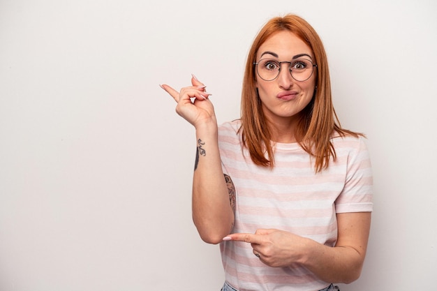 Jonge blanke vrouw geïsoleerd op een witte achtergrond geschokt wijzend met wijsvingers naar een kopie ruimte.