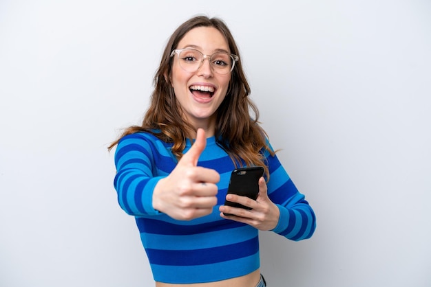 Jonge blanke vrouw geïsoleerd op een witte achtergrond met behulp van mobiele telefoon terwijl het doen van thumbs up