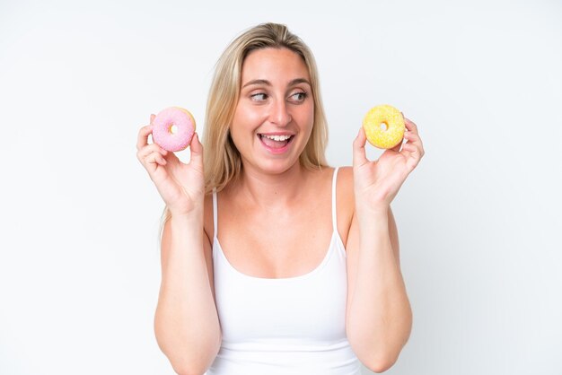 Jonge blanke vrouw geïsoleerd op een witte achtergrond met donuts en verrast