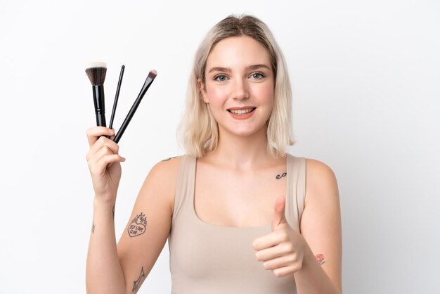 Jonge blanke vrouw geïsoleerd op een witte achtergrond met make-up borstel en met duim omhoog