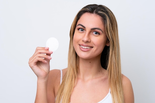 Jonge blanke vrouw geïsoleerd op een witte achtergrond met wattenschijfje voor het verwijderen van make-up van haar gezicht en glimlachen