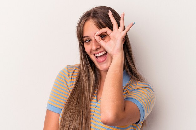 Jonge blanke vrouw geïsoleerd op een witte achtergrond opgewonden houden ok gebaar op oog.