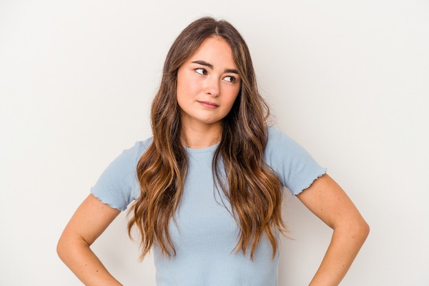 Jonge blanke vrouw geïsoleerd op een witte achtergrond verward, voelt zich twijfelachtig en onzeker.