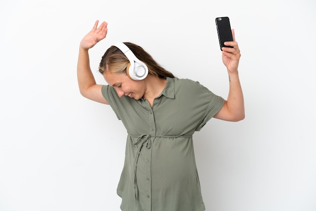 Jonge blanke vrouw geïsoleerd op een witte achtergrond zwanger en dansen tijdens het luisteren naar muziek