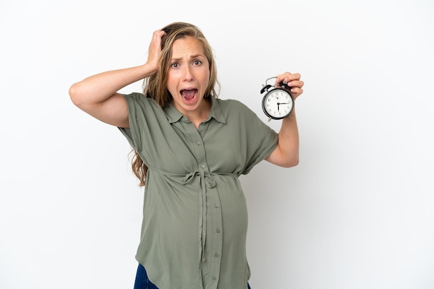 Foto jonge blanke vrouw geïsoleerd op een witte achtergrond zwanger en houden klok met verbaasde expression