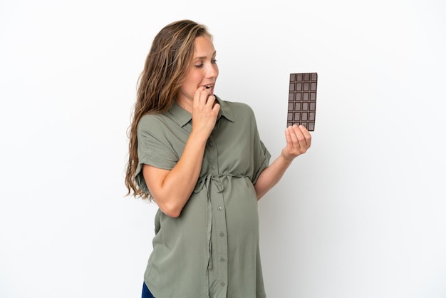 Jonge blanke vrouw geïsoleerd op een witte achtergrond zwanger en twijfels terwijl ze chocolade vasthoudt