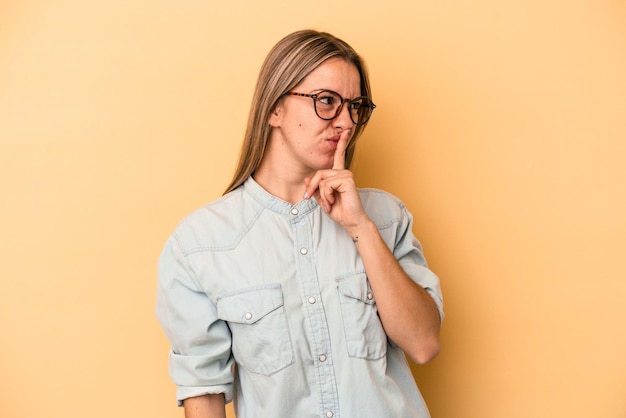 Jonge blanke vrouw geïsoleerd op gele achtergrond die een geheim houdt of om stilte vraagt.