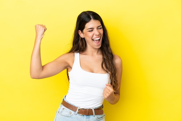 Jonge blanke vrouw geïsoleerd op gele achtergrond die een overwinning viert