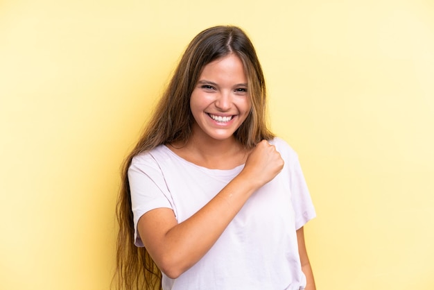 Jonge blanke vrouw geïsoleerd op gele achtergrond die een overwinning viert