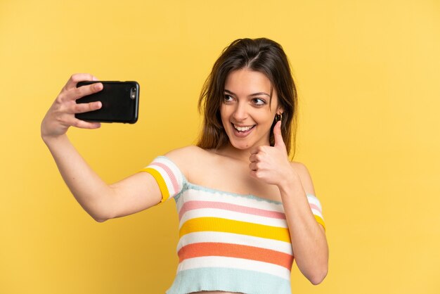 Jonge blanke vrouw geïsoleerd op gele achtergrond die een selfie maakt met mobiele telefoon