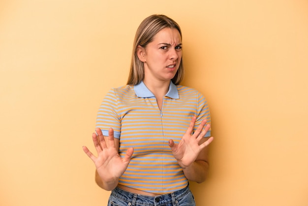 Jonge blanke vrouw geïsoleerd op gele achtergrond die iemand afwijst die een gebaar van walging toont.