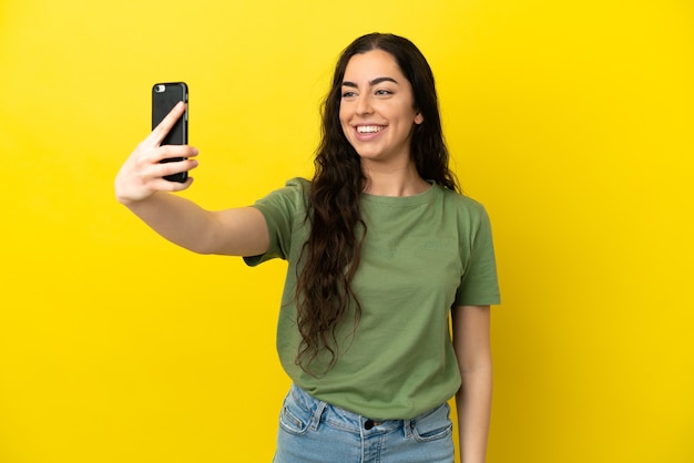 Jonge blanke vrouw geïsoleerd op gele achtergrond een selfie maken
