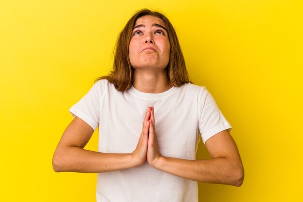 Jonge blanke vrouw geïsoleerd op gele achtergrond hand in hand bidden in de buurt van mond, voelt zich zelfverzekerd.
