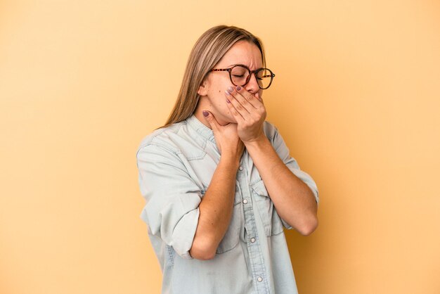 Jonge blanke vrouw geïsoleerd op gele achtergrond lijdt aan pijn in de keel als gevolg van een virus of infectie.