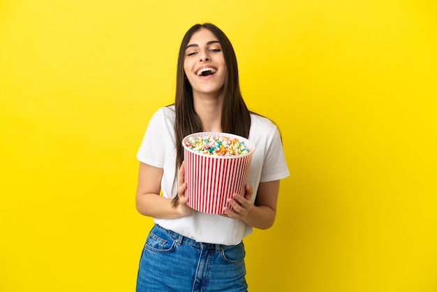 Jonge blanke vrouw geïsoleerd op gele achtergrond met een grote emmer popcorns