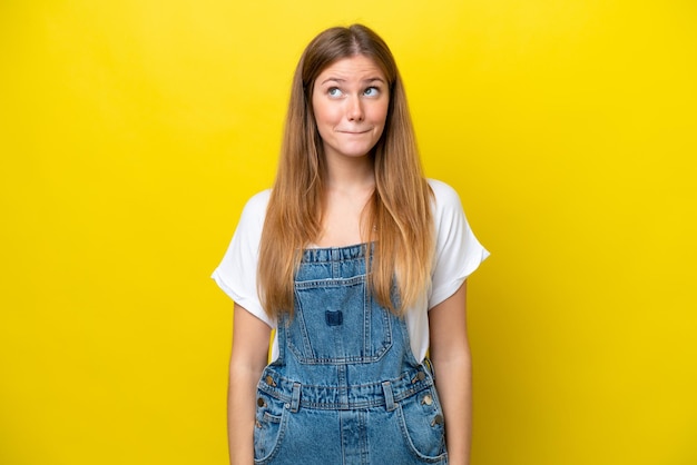 Jonge blanke vrouw geïsoleerd op gele achtergrond twijfels tijdens het kijken